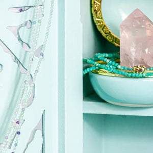 Open image in slideshow, on the left, hanging on cabinet door, 1mm fluorite faceted crystal necklace. on the right, inside cabinet, 2mm amazonite necklace around rose quartz point in jewelry box. close-up.

