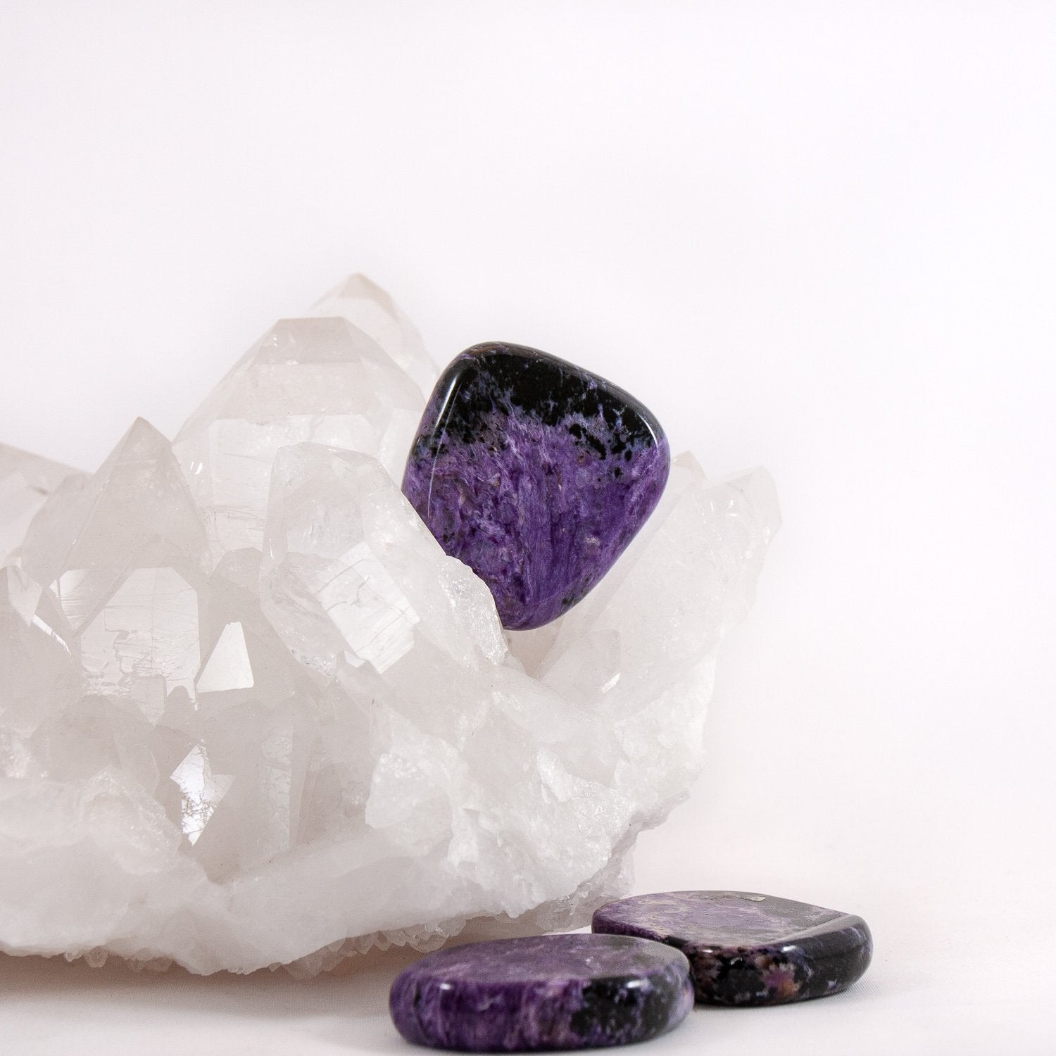 Charoite flat stones. One sitting on quartz cluster, two lying in front of it.