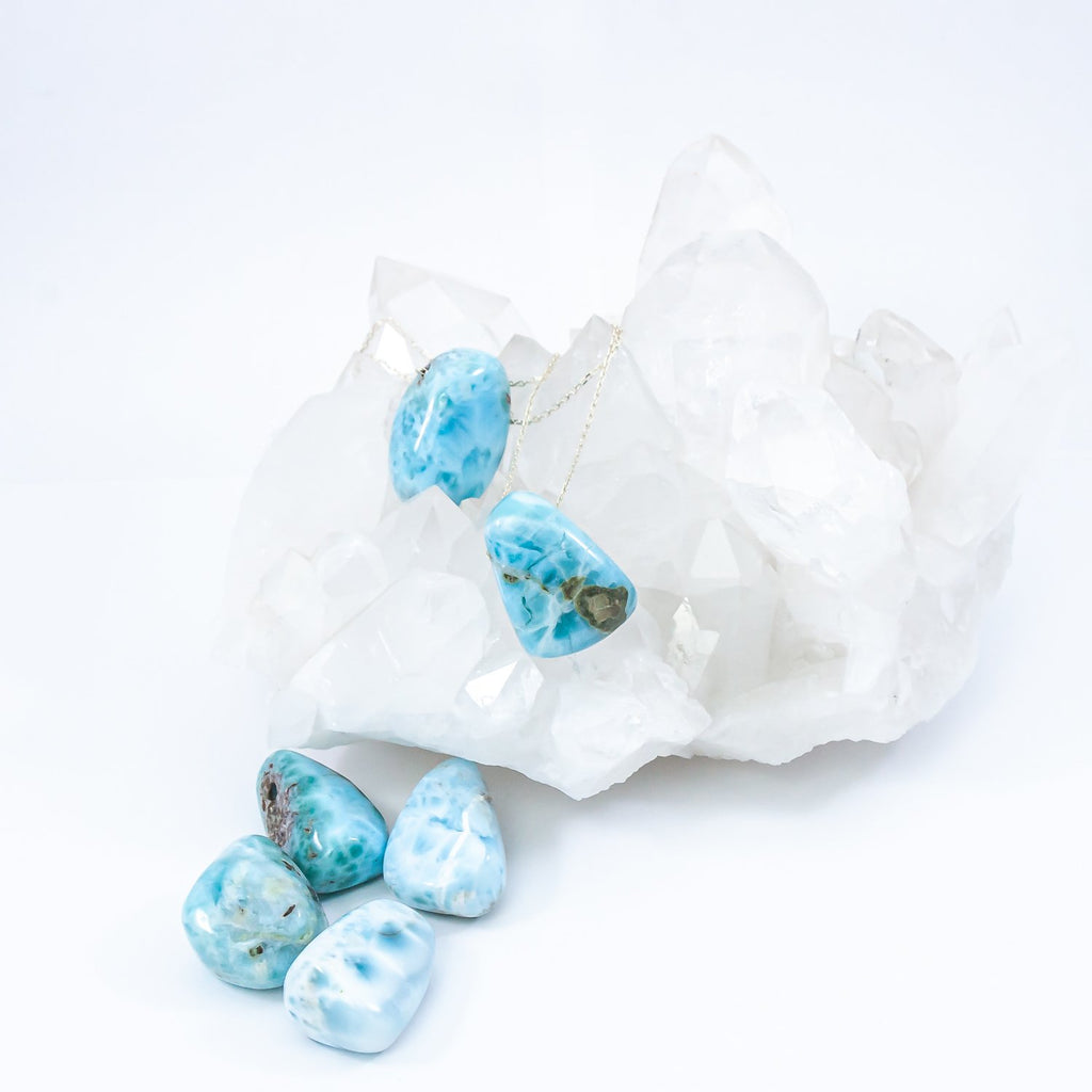 larimar crystal drop pendant necklaces. sitting on top and in front of quartz crystal cluster.