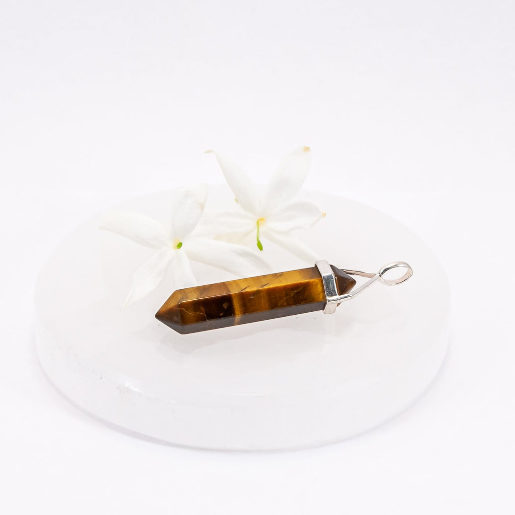Tiger's eye crystal pendant sitting on selenite plate with flowers.