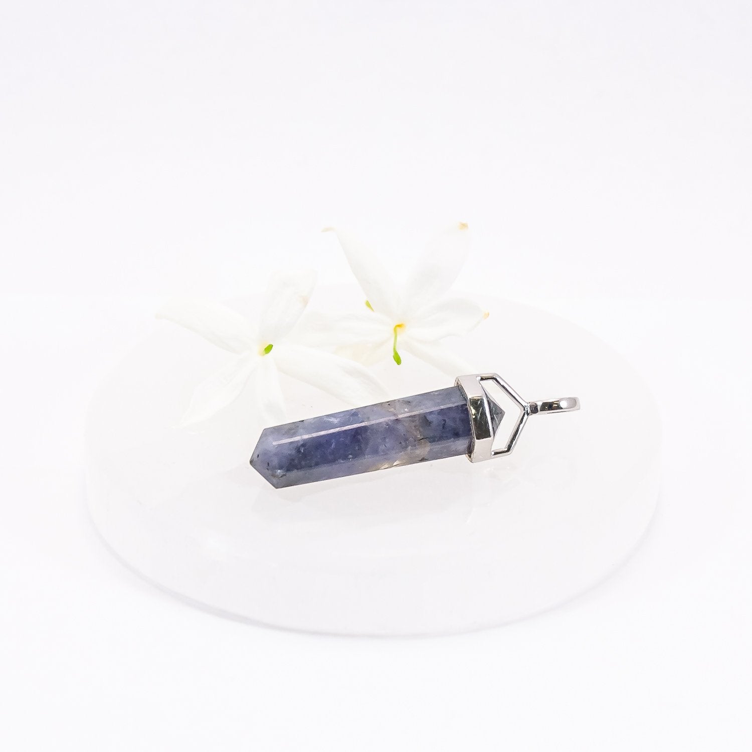 Tanzanite crystal pendant sitting on selenite plate with flowers.