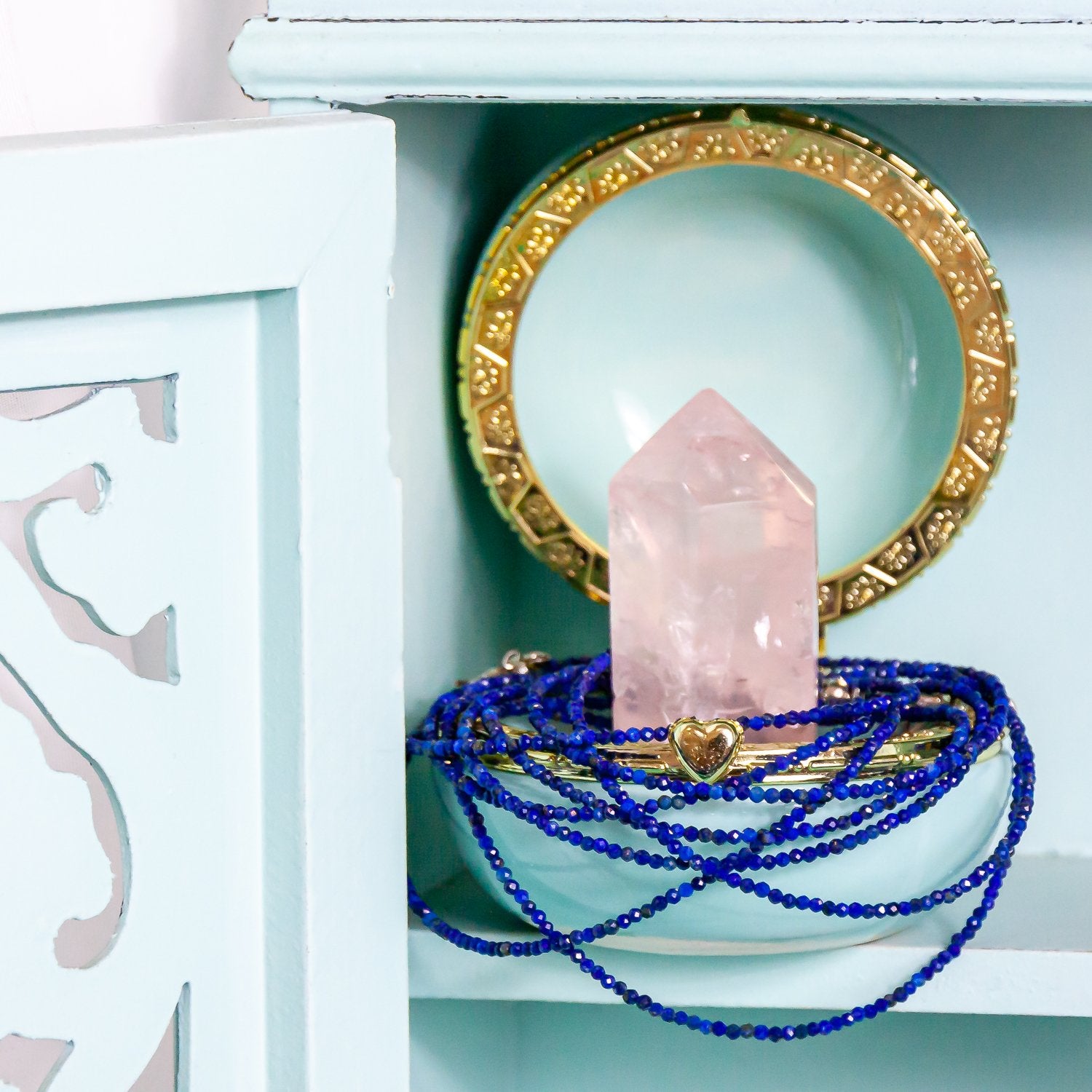 1mm lapis lazuli faceted crystal necklace around rose quartz point, inside jewelry box. all inside cabinet. close-up.