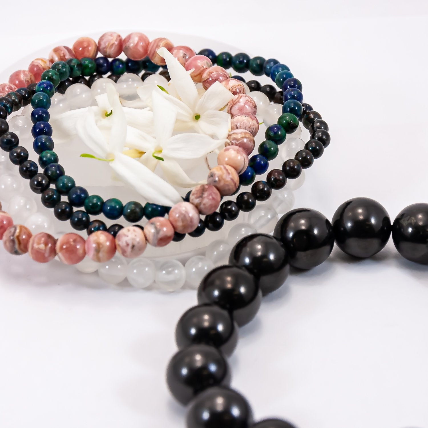 Shungite purification bracelet. Selenite, chrysocolla, azurite, and rhodochrosite beaded bracelets around white flowers.