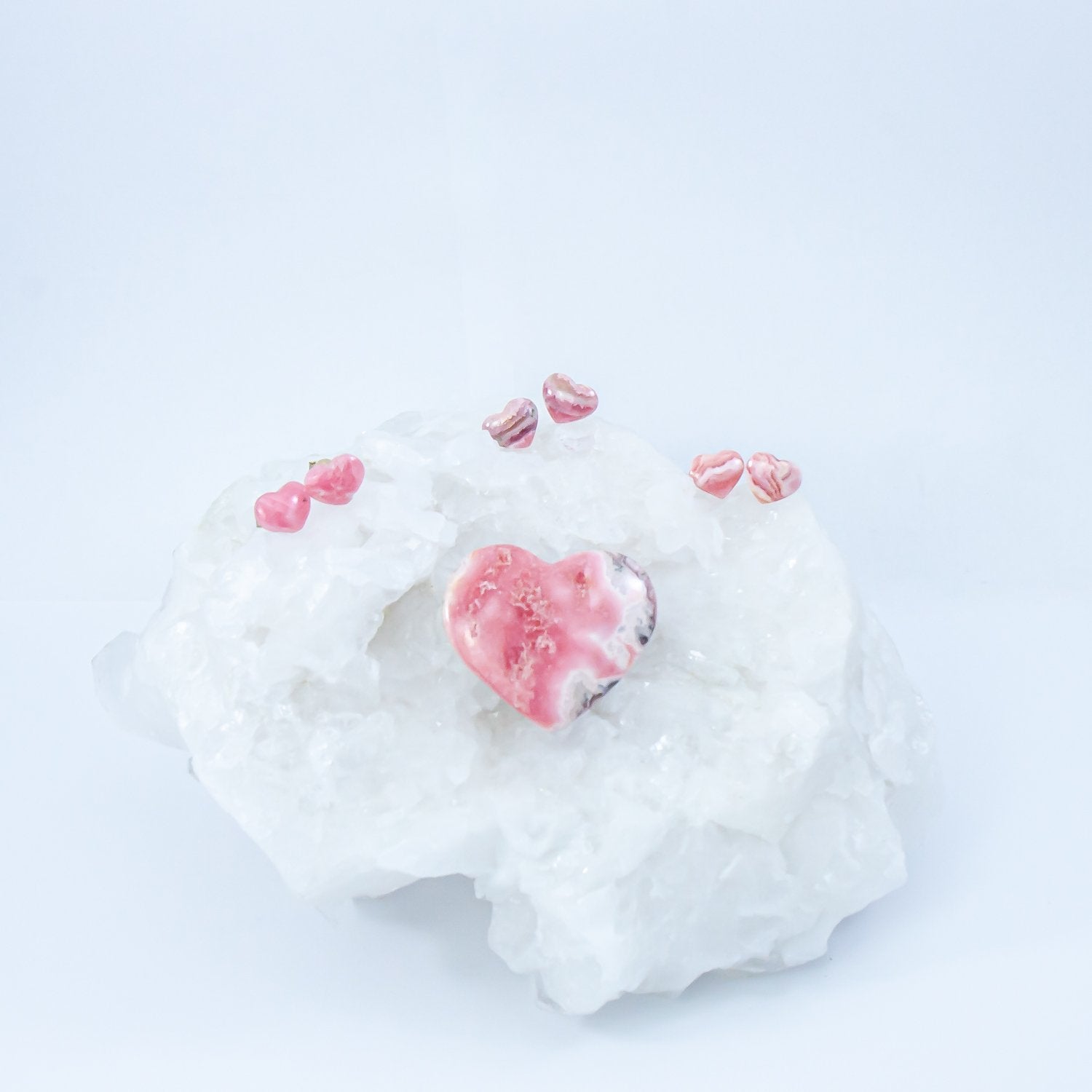 rhodochrosite heart crystal earrings atop a quartz crystal with another rhodochrosite heart stone.