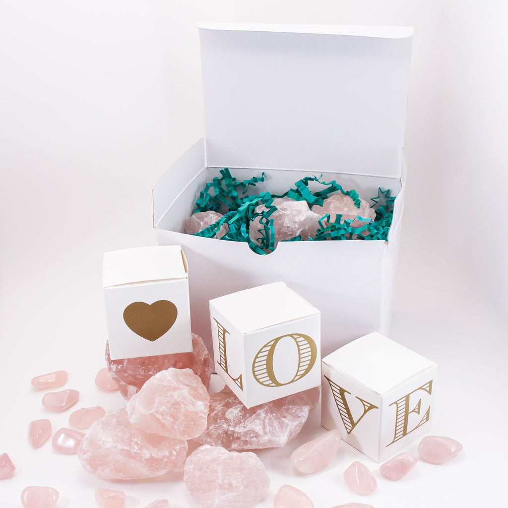rose quartz box of love. raw rose quartz in a box surrounded by more raw rose quartz, rose quartz tumbled stones, and additional boxes, spelling LOVE.