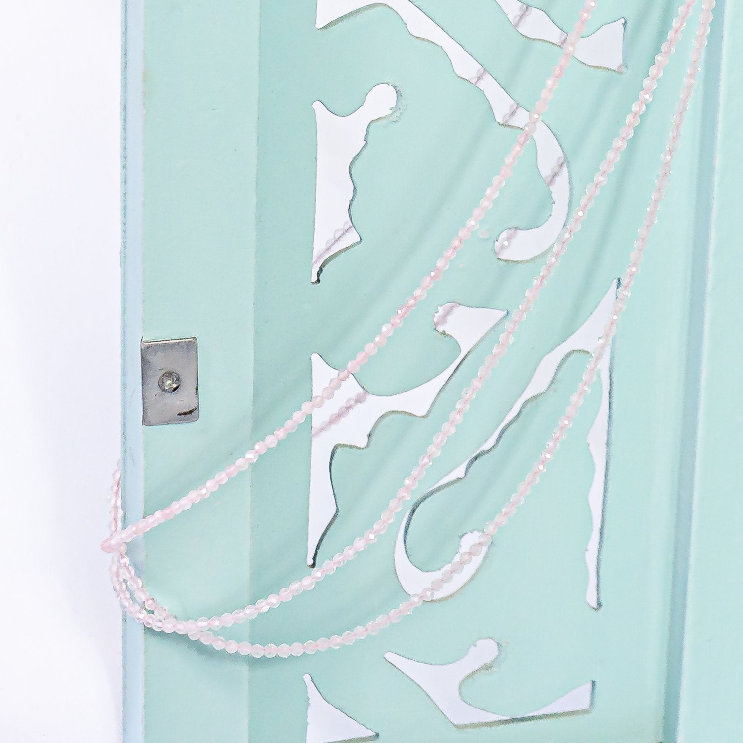 1mm rose quartz faceted crystal necklace hanging on jewelry cabinet door.