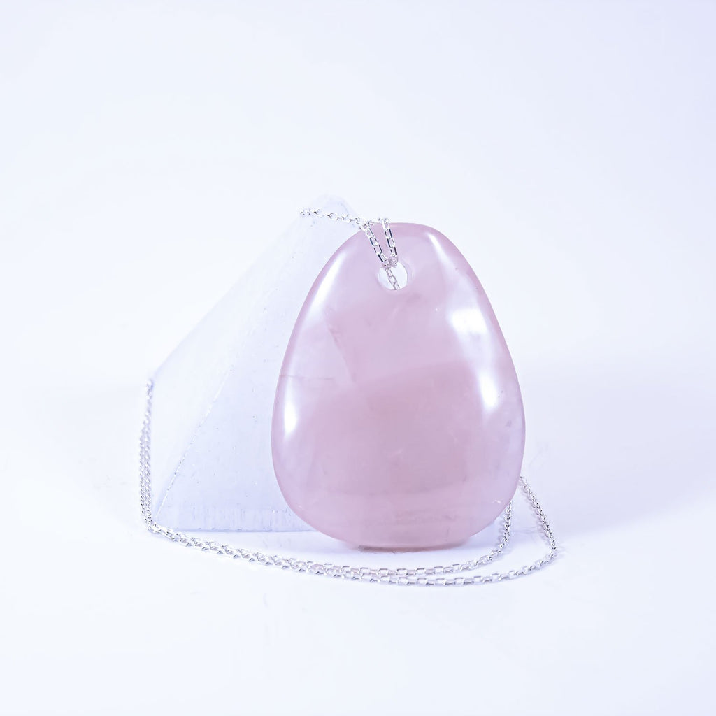 rose quartz crystal drop pendant necklace. sterling silver chain. leaning on selenite pyramid.
